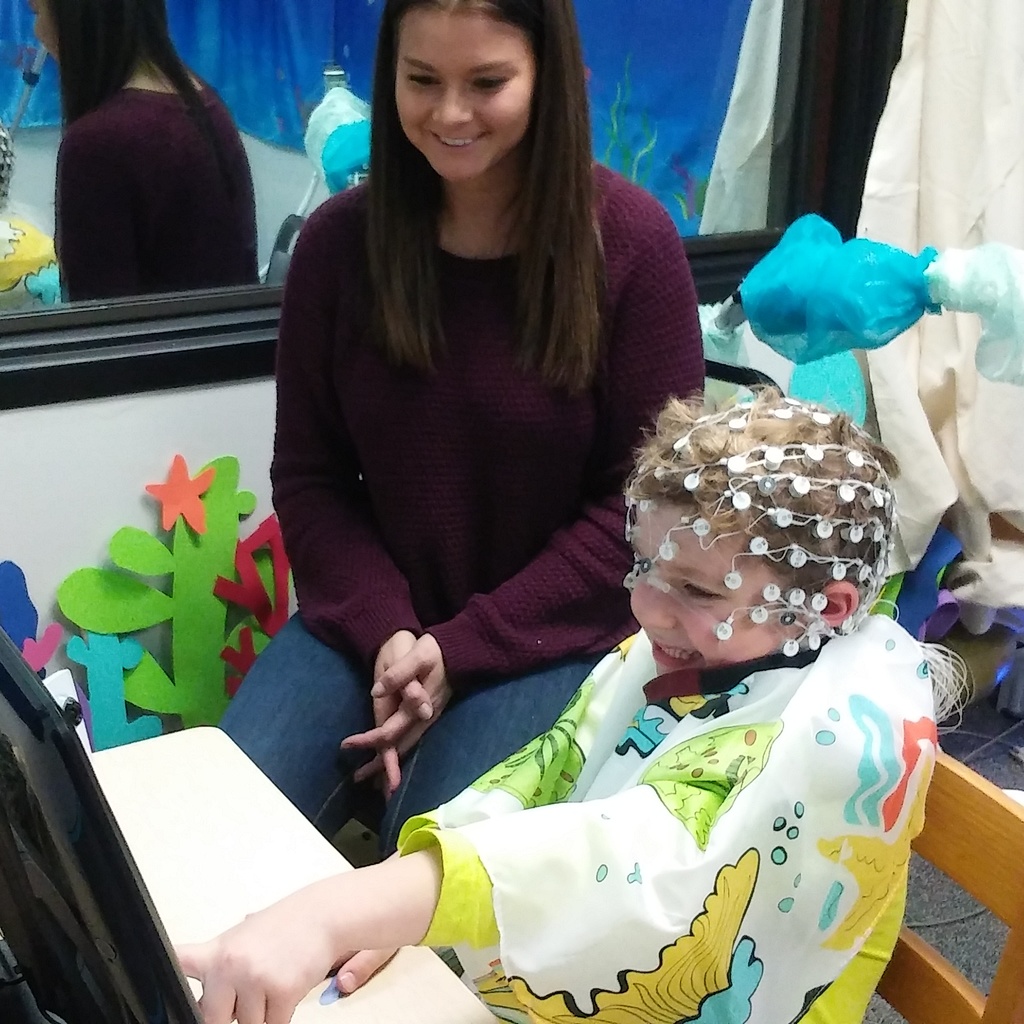 Child and researcher playing a game with an EEG cap on.